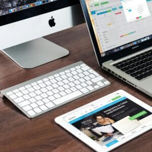 A sleek office desk setup featuring Apple devices: iMac, MacBook, and iPad.