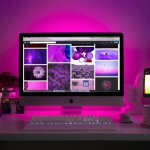 Modern desk setup with neon lighting and a desktop computer displaying colorful images.