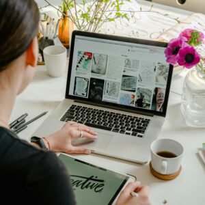 Woman in a creative workspace using a laptop and tablet for calligraphy. Artistic and tech-driven environment.