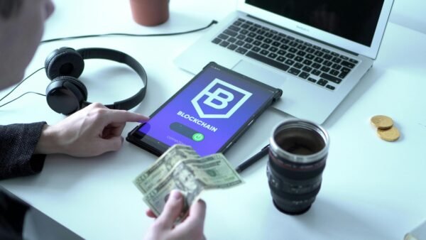 Tablet with blockchain app, laptop, and dollar bills on desk depicting digital finance.